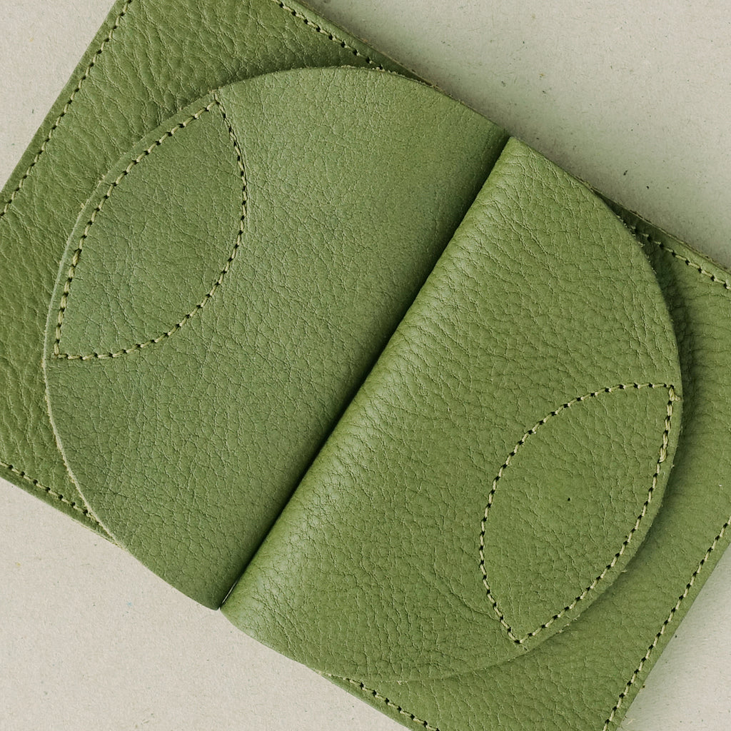 two olive green leather wallets with round flaps, in a flat lay composition