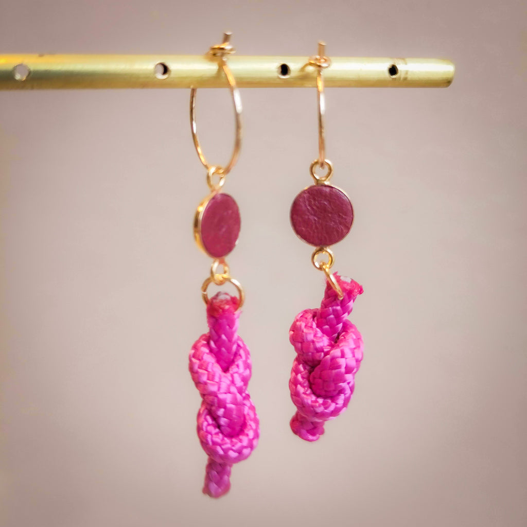 gold dangle earrings with a round shape on top, and dangling knots of rope beneath